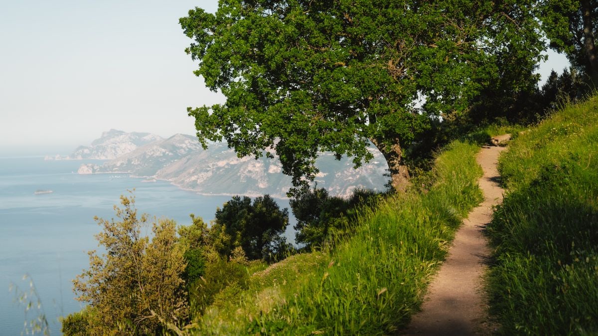 Explore a serene coastal trail with lush greenery and panoramic views in Praiano, Italy.